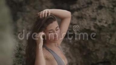 在热带的岩石上穿着刺鼻的泳衣的年轻女子